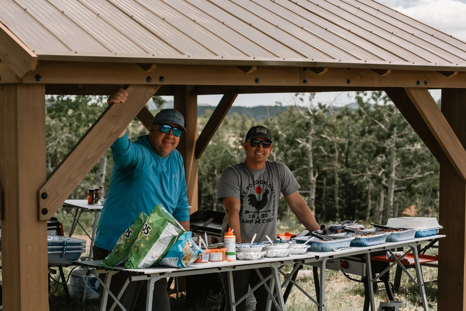 Two people preparing a meal beneath an open-air shelter